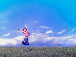 Illustratie: foto van een jonge vrouw die lachend in de lucht springt. De foto hoort bij de pagina over zelfwaardering en zelfrespect en is gemaakt door Marcy Kellar.